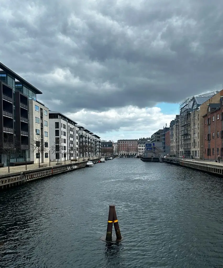 Canal under Clouds, Copenhagen Calm canal lined with modern apartment buildings under a dramatic cloudy sky, Copenhagen