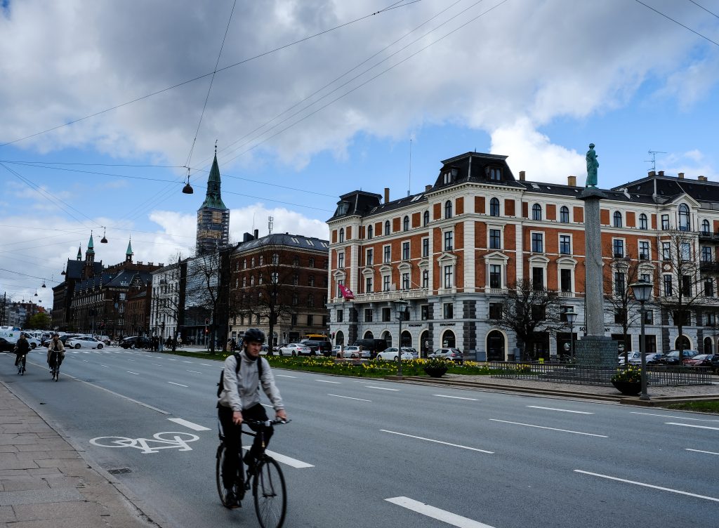 Copenhagen by Bike Cyclist riding along a wide Copenhagen street lined with historic buildings and a church spire