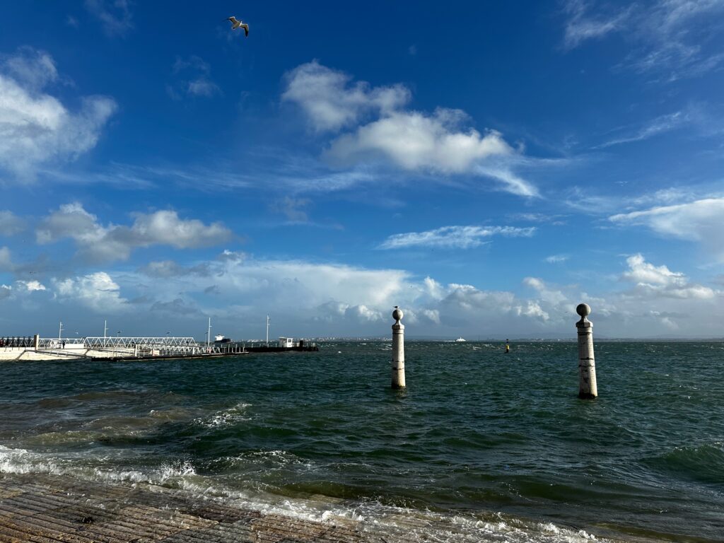 Waves on the Tagus River by the Cais das Colunas pillars under a bright blue sky, Lisbon
