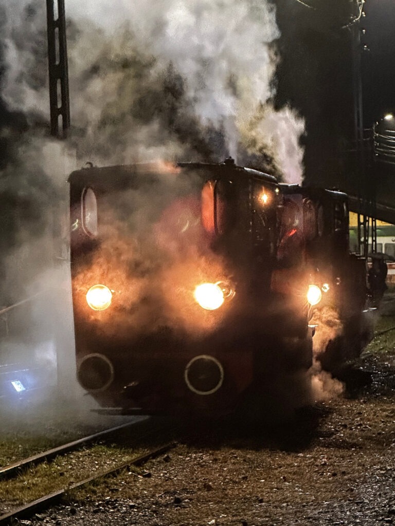 Night Arrival Narrow-gauge steam locomotive with glowing headlamps arriving in a cloud of steam at night, Bytom
