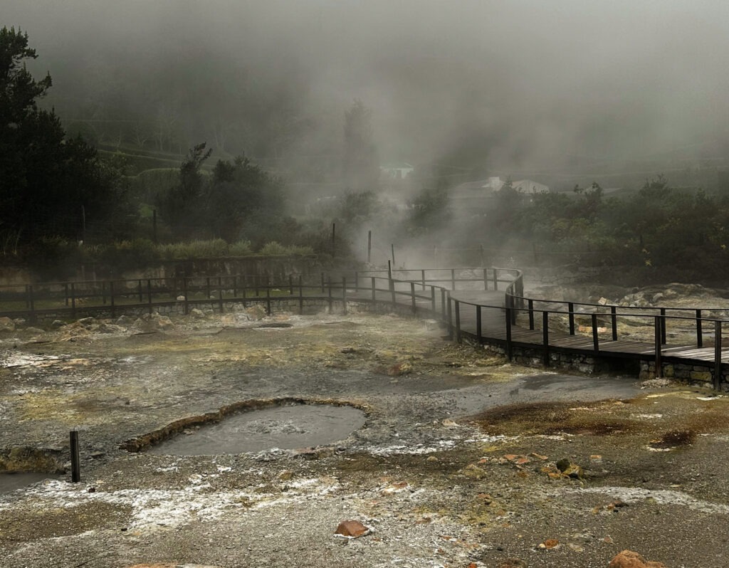 Steam rising from volcanic hot springs beside a wooden boardwalk, Azores