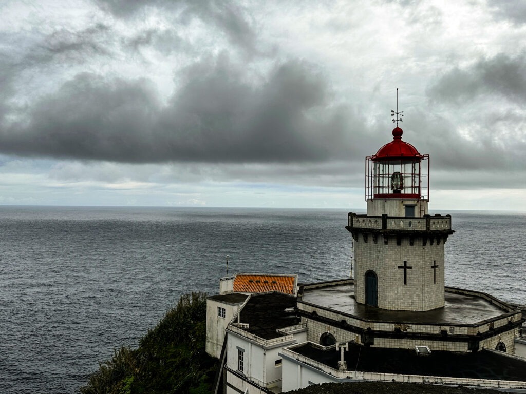 White lighthouse with a red lantern above the Atlantic under heavy clouds, Azores