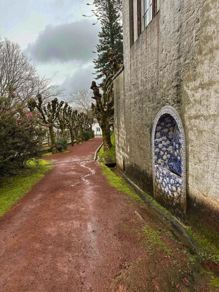 Red dirt path along a whitewashed wall with a blue azulejo tile panel, Azores