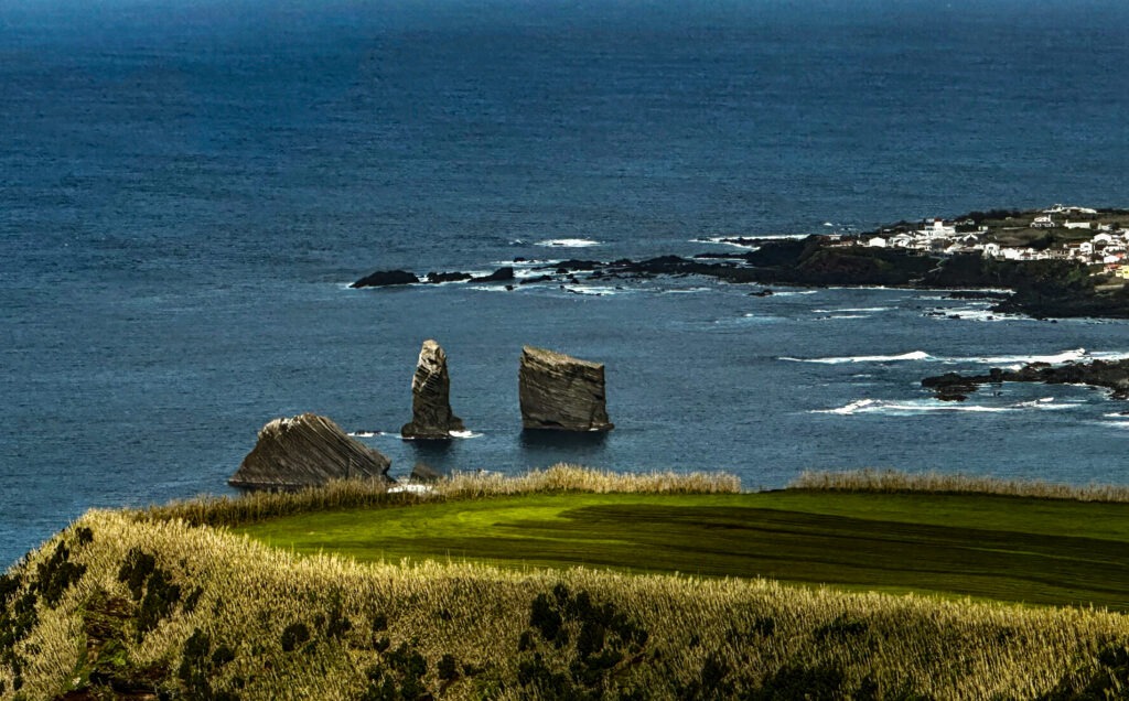 Rock stacks rising from the Atlantic off a green coastal field, Azores