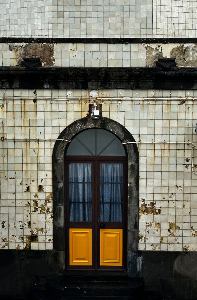 Weathered azulejo-tiled facade with an arched wooden door, Azores