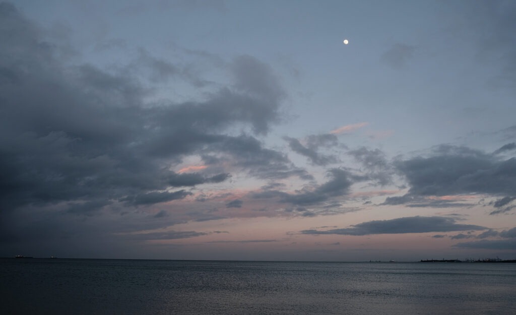 Darkening sea and cloudy sky with a pale moon above the horizon, minimalist fine art seascape