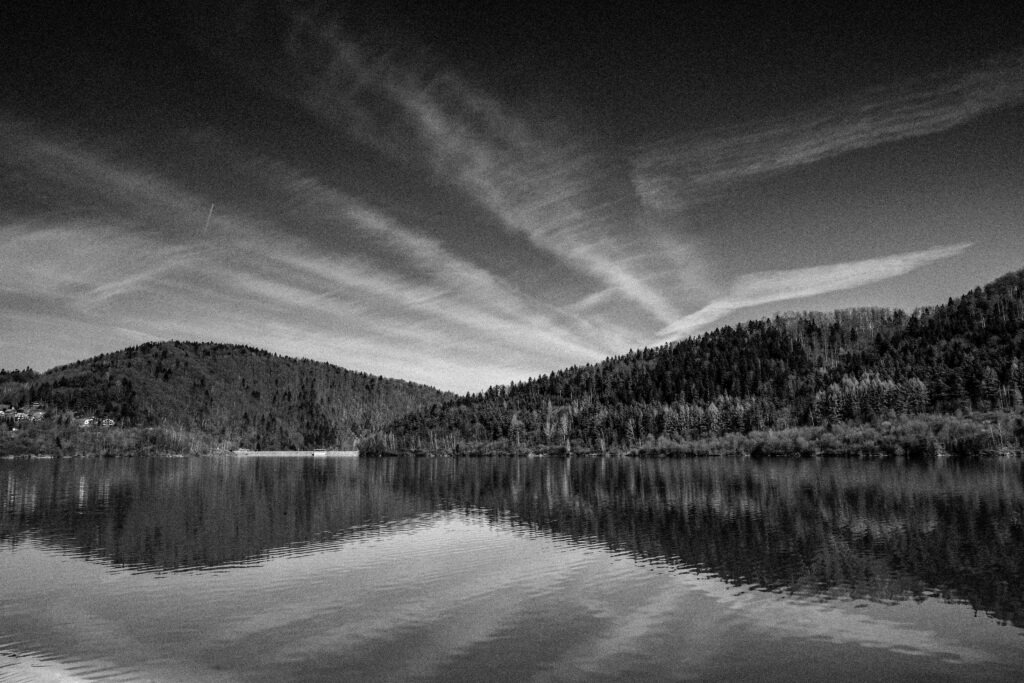 Lake reflecting streaked clouds and distant forested hills, black and white fine art landscape