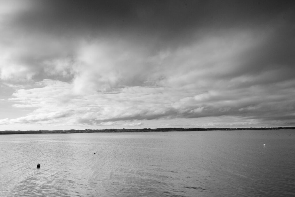 Wide minimalist horizon over calm water under dramatic clouded sky, black and white fine art landscape photography