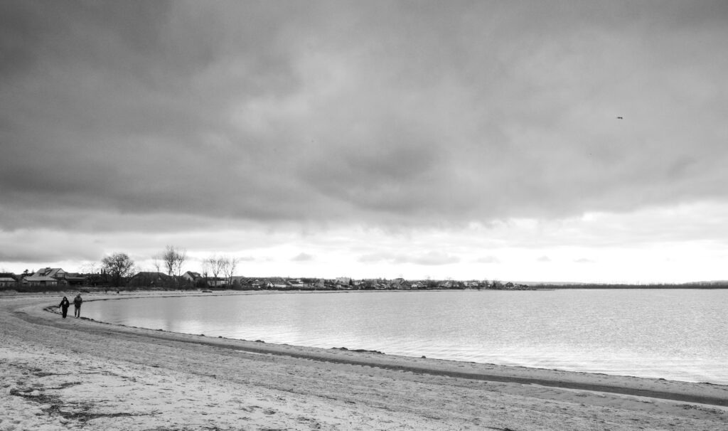 Soft shoreline fading into misty horizon under a wide cloudy sky, black and white landscape photograph