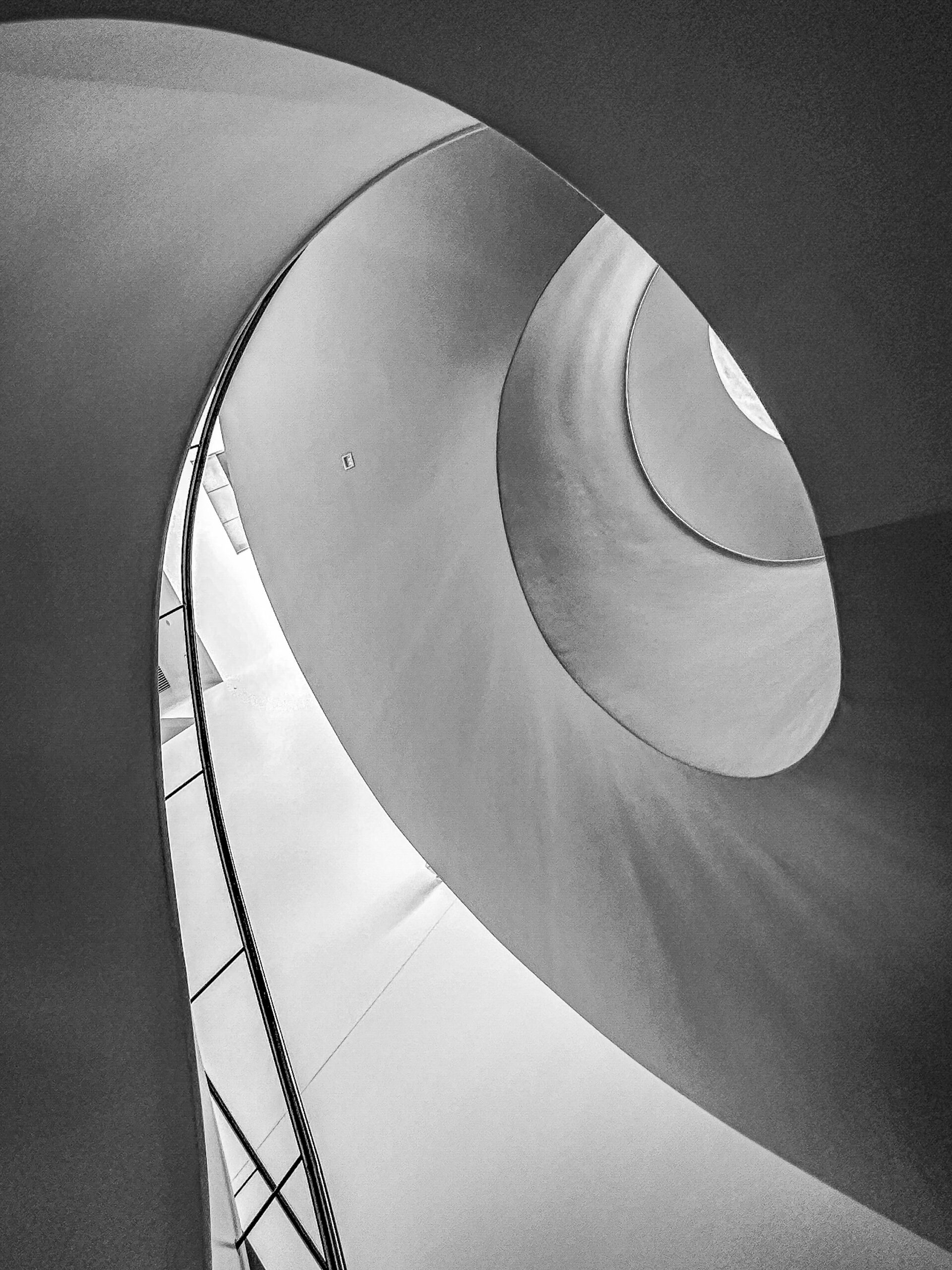 Alt: Flow — curved architecture fine art photography by Andrus Markus Opis: A spiral staircase dissolves into light — movement frozen into pure geometric form.